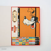 A Disney-themed stationery gift set displayed inside an open red and white box on a white background. The set includes an orange notebook with a Goofy illustration, several colorful pencils, a cream Mickey Mouse pencil sharpener, a a red point guard.
