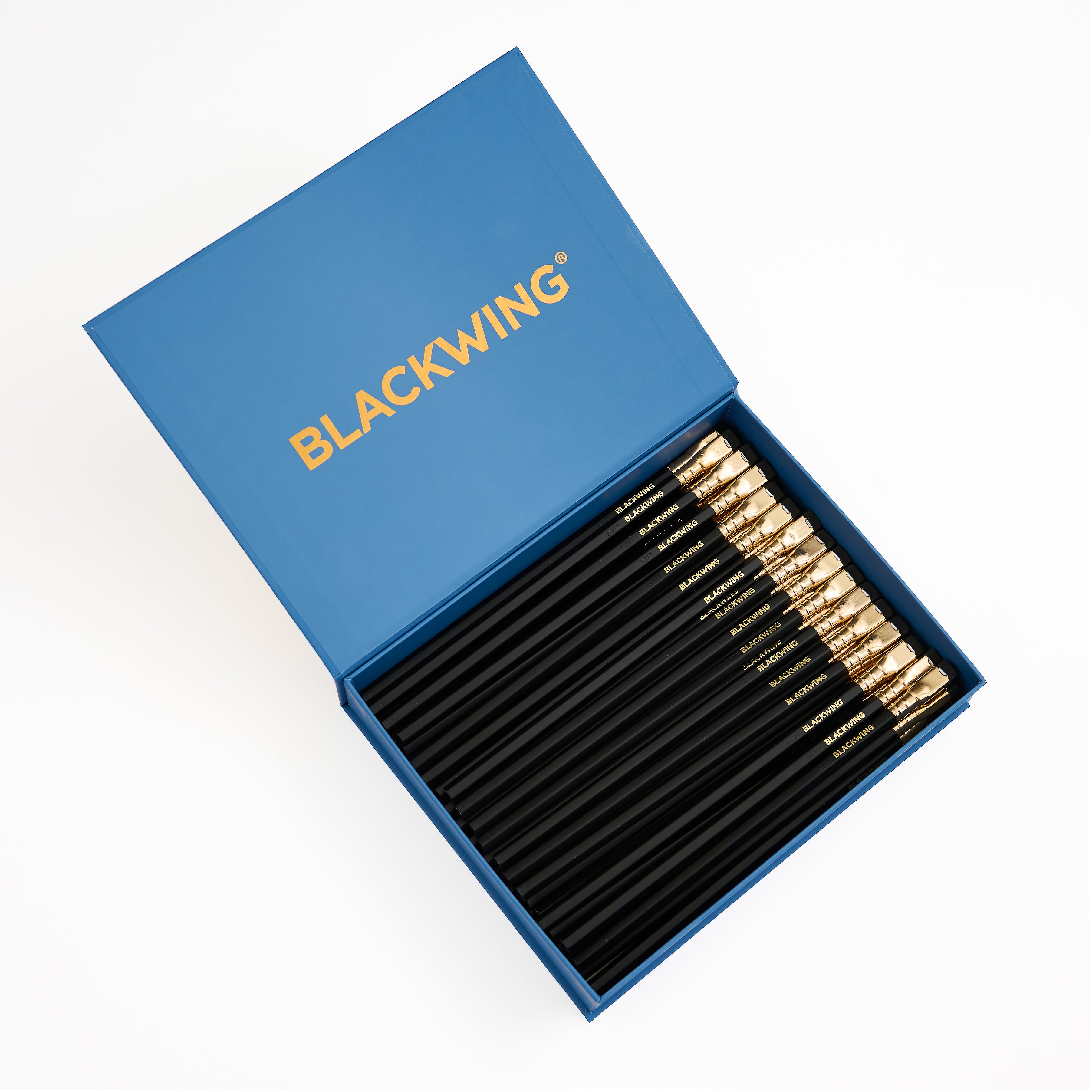 A set of black wood pencils with gold ferrules, black eraser, and gold BLACKWING imprint, neatly arranged inside an open blue presentation box with the brand name BLACKWING printed in gold on the lid, shot on a clean white background.