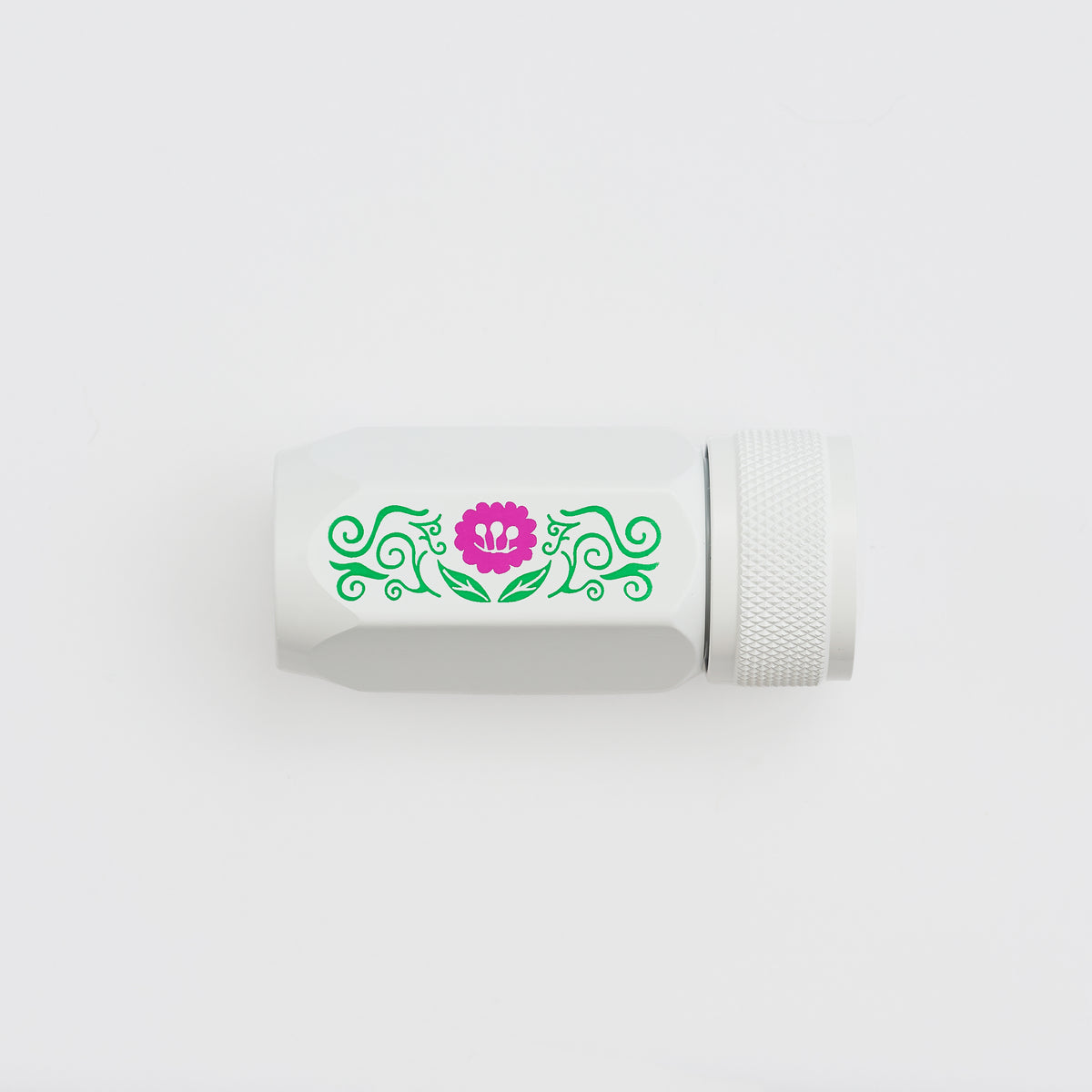 A white cylindrical pencil sharpener with a textured screw-on cap, featuring a decorative green scroll pattern and a pink flower graphic on the side, set against a plain white background.