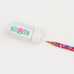 A white pencil sharpener with a green and pink floral design, shown next to a colorful pencil on a clean white background.