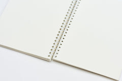 An open blank spiral notebook with cream-colored pages and a white metal coil binding, photographed on a clean white background.