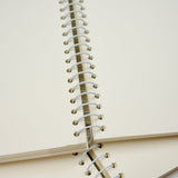 A close-up of a spiral notebook with cream-colored pages and white wire binding, shown with another notebook underneath.