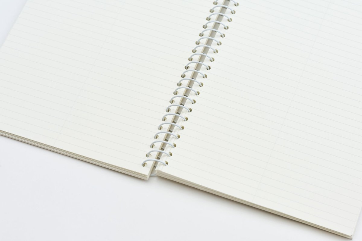 An open spiral-bound lined notebook with cream-colored pages and a white metal coil, photographed on a clean white background.