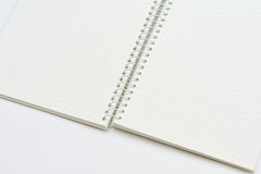 An open spiral-bound lined notebook with cream-colored pages and a white metal coil, photographed on a clean white background.