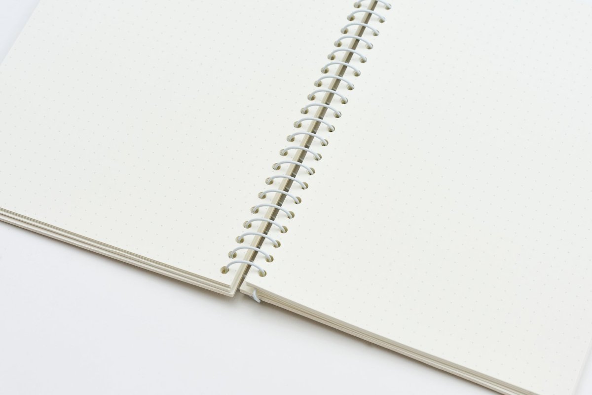 An open spiral-bound notebook with blank, warm off-white pages and a white metal coil binding, photographed on a clean white background.