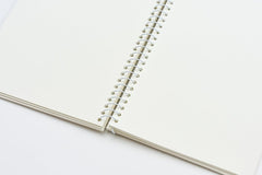 An open spiral-bound notebook with blank, warm off-white pages and a white metal coil binding, photographed on a clean white background.