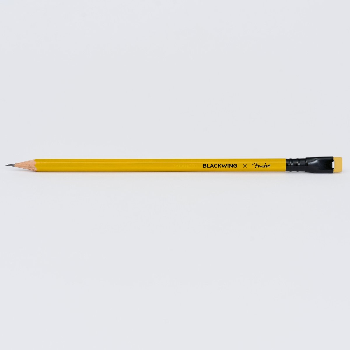 A sharpened yellow Blackwing x Fender pencil with a black ferrule and yellow eraser, shown horizontally against a light background.