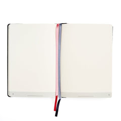 An open Blackwing planner with blank cream-colored pages, held open by one pink and one grey ribbon bookmarks with, on a solid white background.