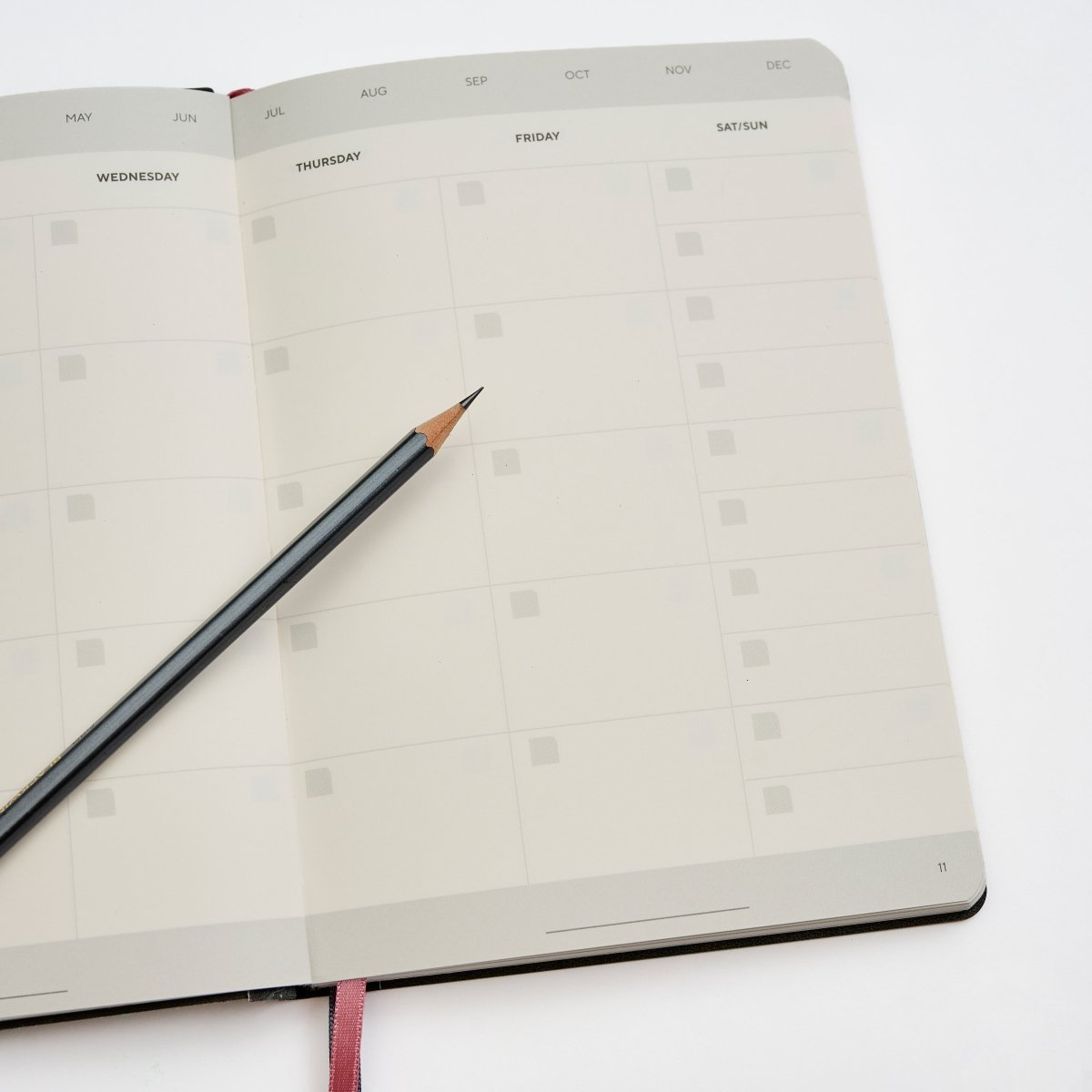 An open Blackwing Planner showing blank weekly calendar pages photographed on a clean white background with a Blackwing 602 Pencil resting across the pages.