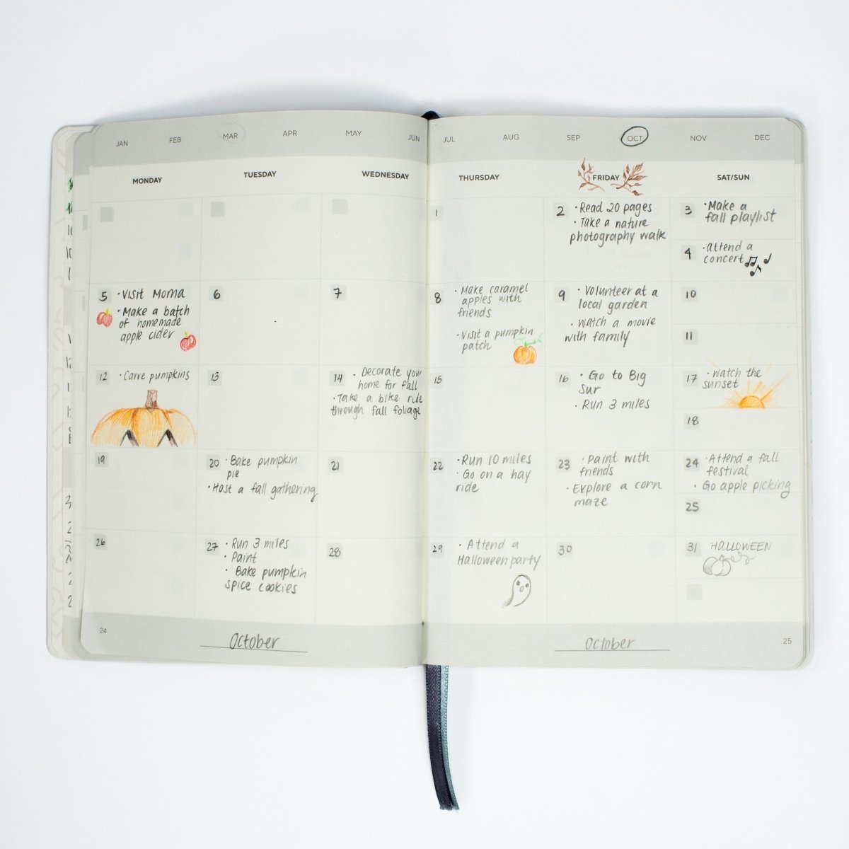 Open Blackwing Planner showing a filled-in monthly calendar spread with handwritten notes, small drawings, and a grey ribbon bookmark against a white background.