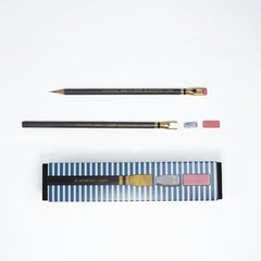 Two dark grey pencils with gold ferrules and pink erasers, shown alongside their blue-and-white striped packaging on a clean white background.