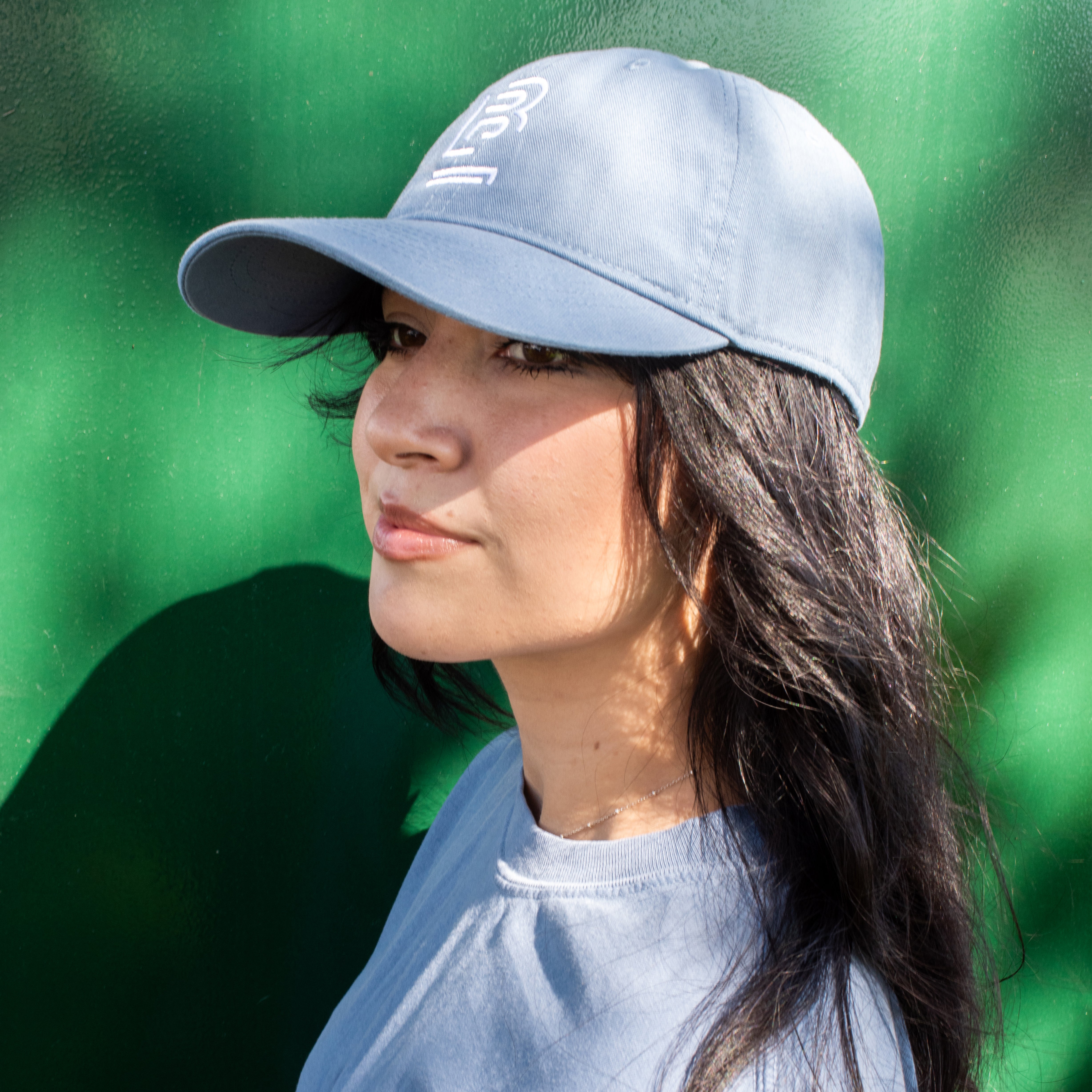 side profile of a woman wearing a blue baseball cap and blue t-shirt against a green background