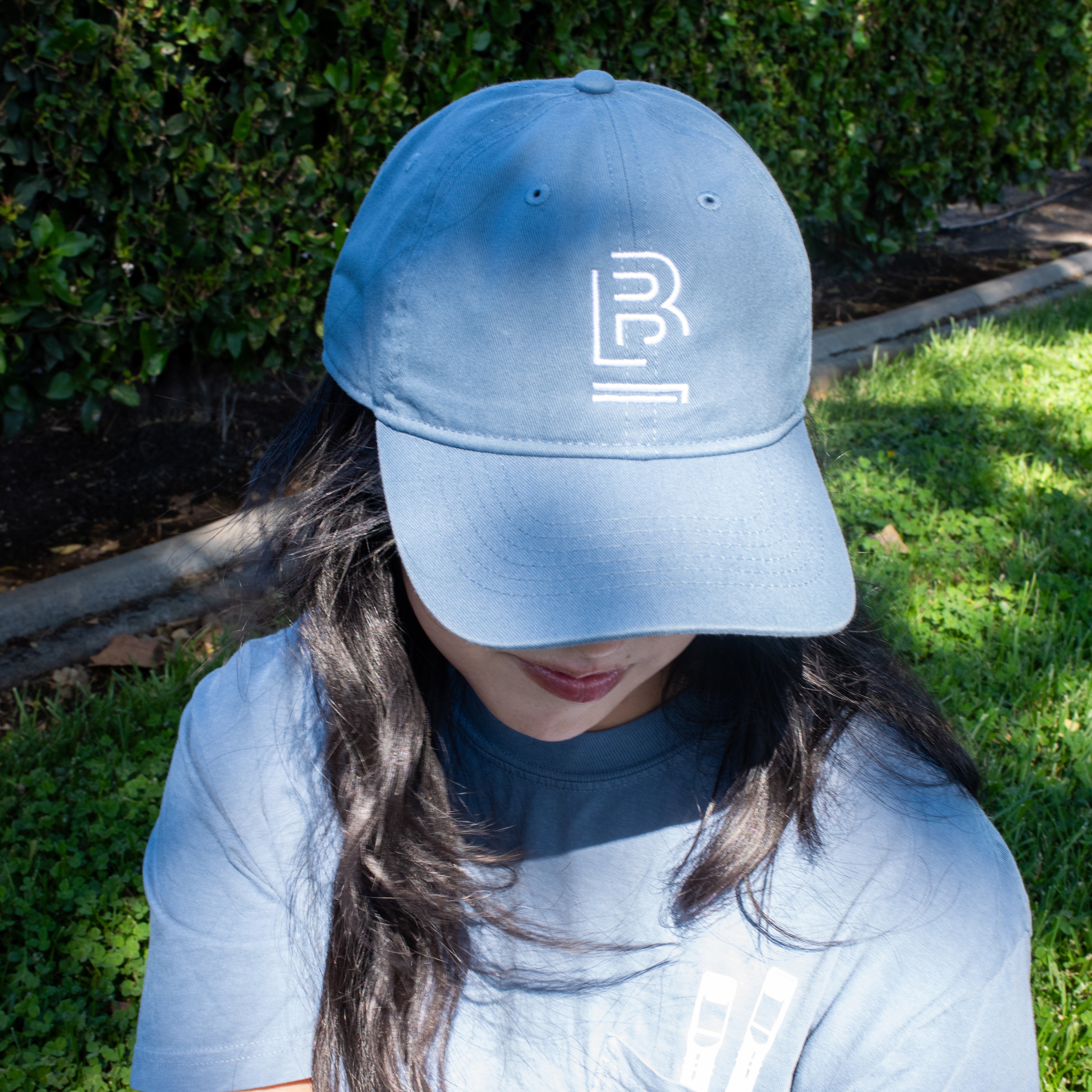 person sitting on the grass wearing a blue baseball cap with 'B' emblem stitched on the front and a matching blue t-shirt 