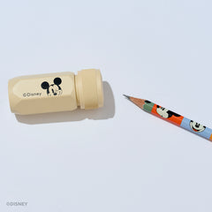 A Disney Mickey Mouse pencil sharpener in a light beige color with a black Mickey graphic and copyright text, shown next to a colorful pencil on a clean white background.