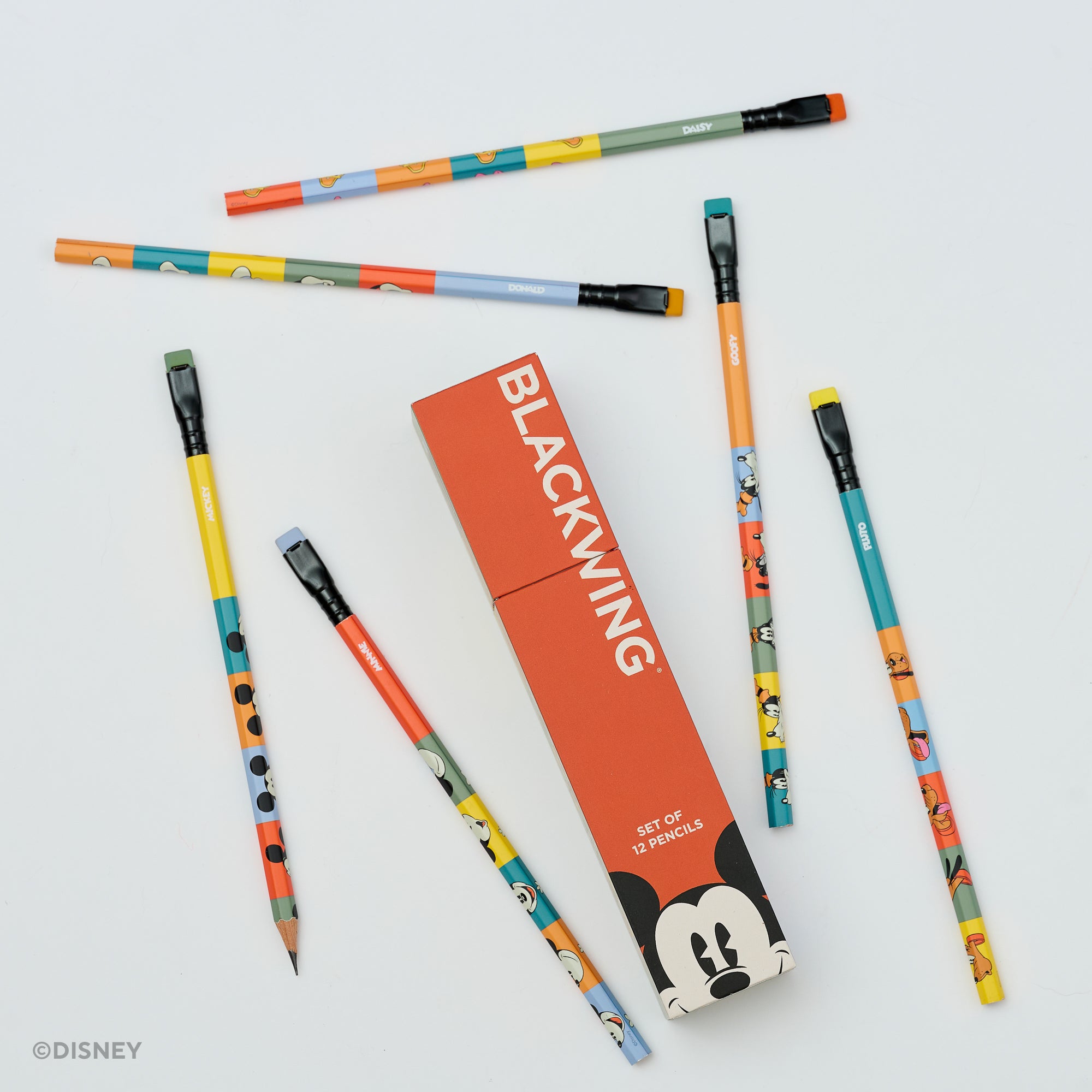 A set of colorful pencils with Disney character illustrations arranged around a red-orange rectangular box labeled BLACKWING on a light gray background. The pencils feature multiple bright colors and cartoon motifs, and the box includes a Mickey Mouse face graphic.