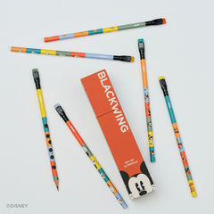 A set of colorful pencils with Disney character illustrations arranged around a red-orange rectangular box labeled BLACKWING on a light gray background. The pencils feature multiple bright colors and cartoon motifs, and the box includes a Mickey Mouse face graphic.