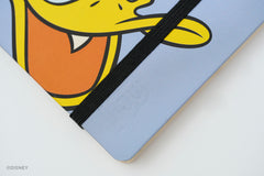 A close-up of a light blue Disney Blackwing notebook with a black elastic closure band and a cartoon Donald Duck face printed on the cover. A Disney watermark is visible in the bottom-left corner.