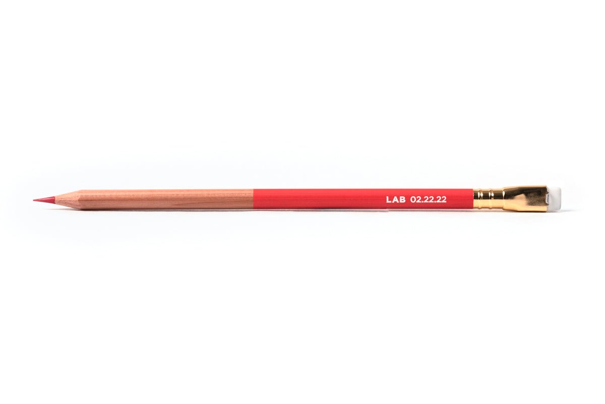 A close-up of a Blackwing Lab 02.22.22 pencil, part natural wood, part red, with red graphite and white eraser
